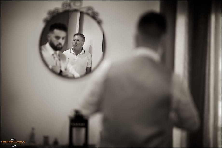 The groom's father, leaning against the wall, while waiting for his son to be ready, in a mirror.