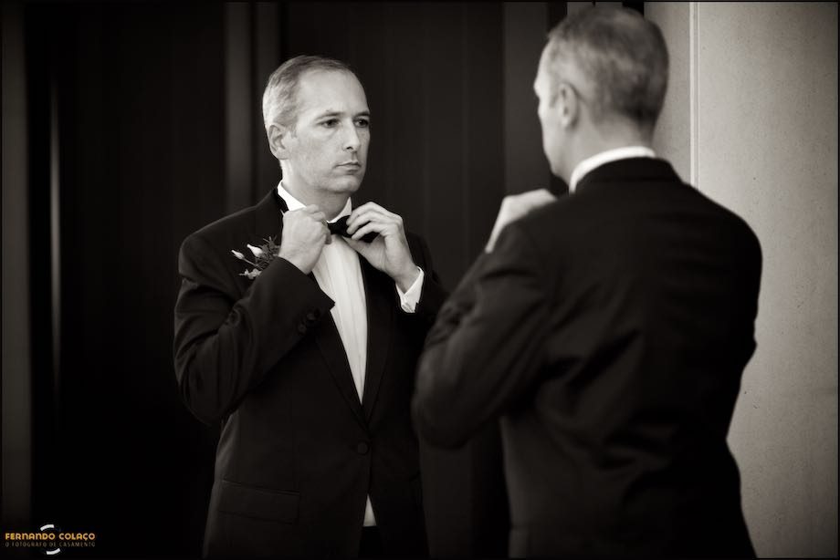 The groom, in the mirror, fixes the lace collar around his neck.