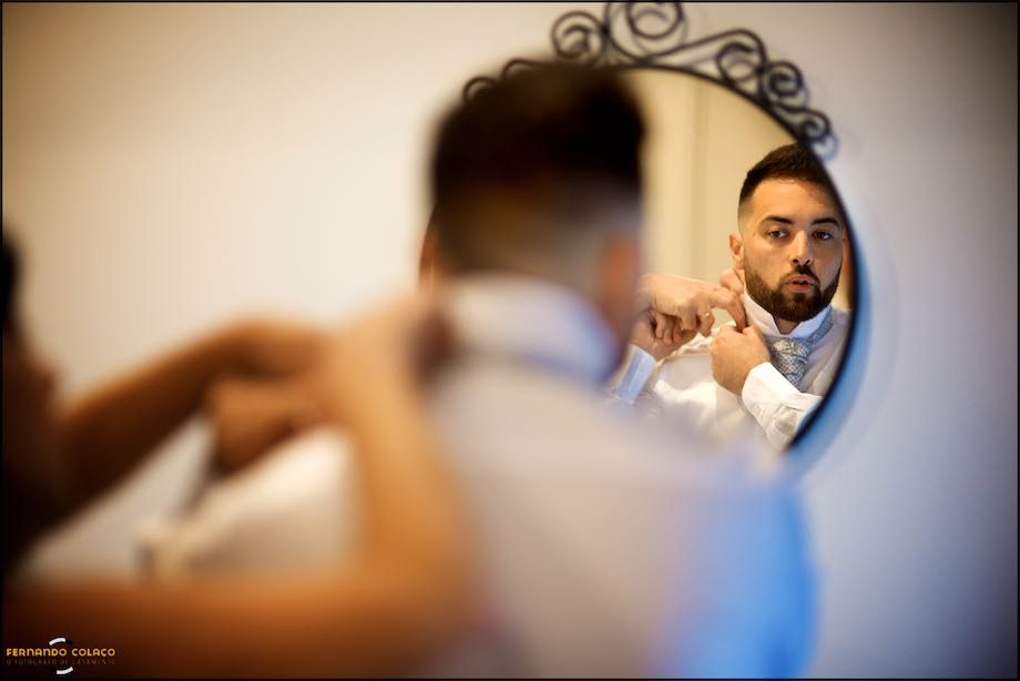 The groom is helped by the mother's hands, inside a round mirror, by the wedding photographer in Portugal.