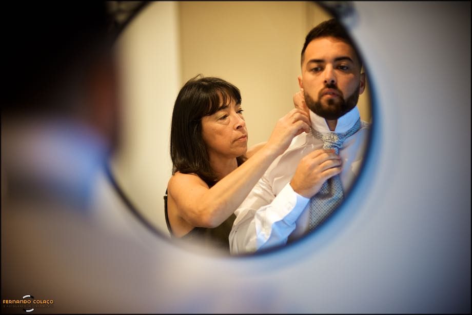 Groom, in the mirror, with his mother who helps him with his tie.