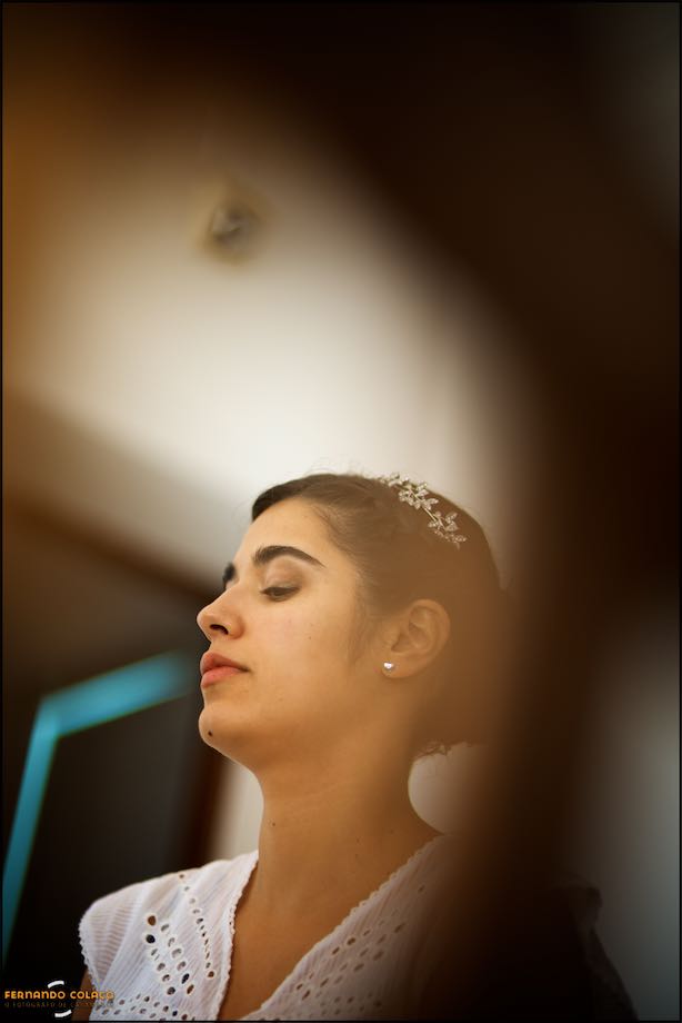 Bride's face and tiara in her hair as she waits, with one arm blurred in the foreground.