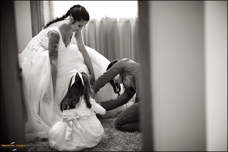 Bride, sitting, while her sister and niece help her with her shoes.