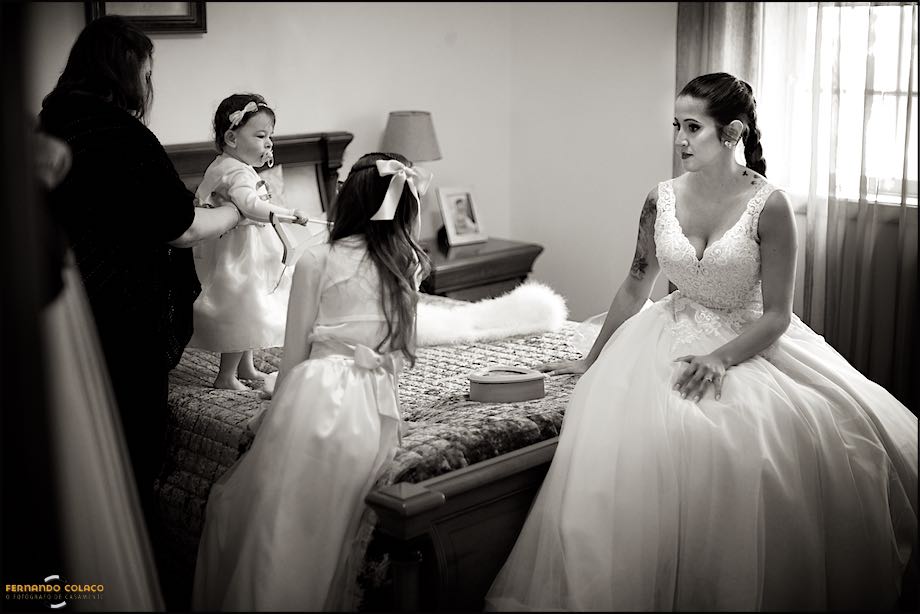 Bride, already ready, sitting on the bed with a girl and another one playing.