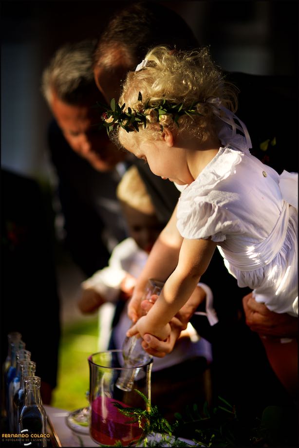 The girl, daughter of the bride and groom, pouring colored sand from a bottle into a large glass.