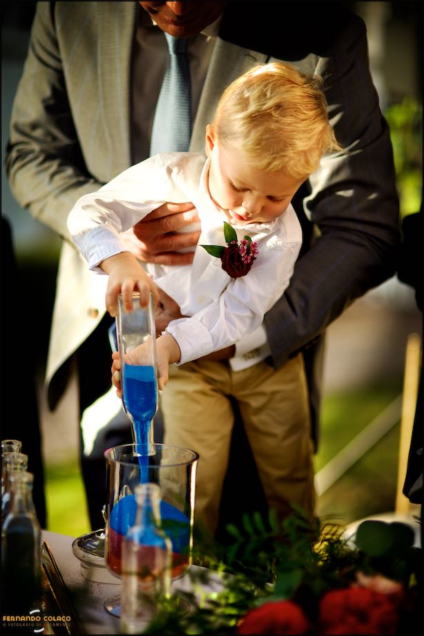 Another of the bride and groom's children pours blue sand into the big glass.