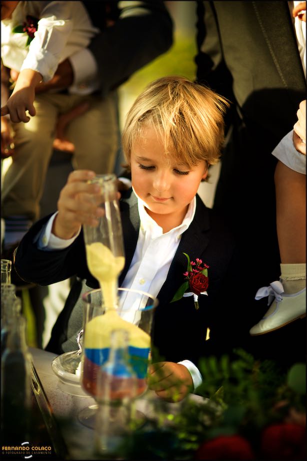 The eldest son of the newly married couple pours yellow sand into the large glass.