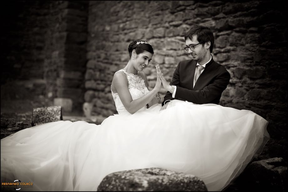 Bride and groom playing together, seated, in the castle of Alandroal, from a wedding in Pirâmides de S.Pedro, in the session with the wedding photographer in Alentejo.