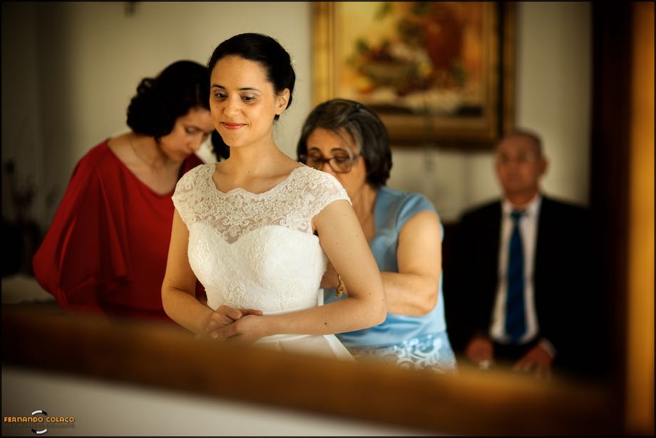 Bride, in a mirror, tightening the dress, by mother and sister and father in the back.