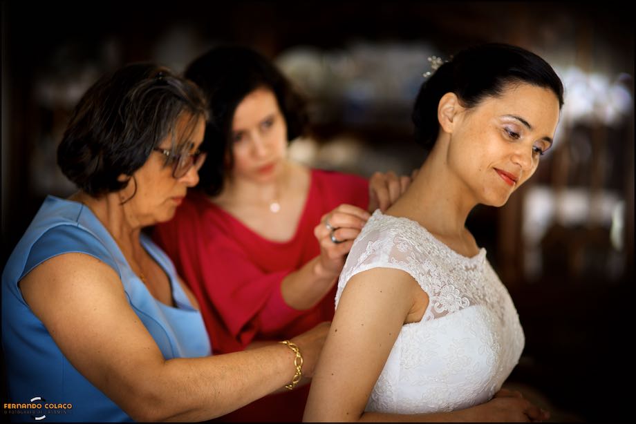 Mother and sister of the bride adjusting the dress with her, smiling.