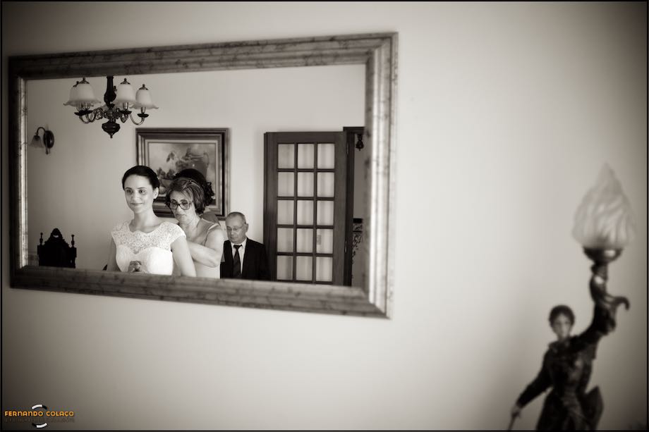 Bride, mother and father in a mirror, with a sculpture lamp on the right.