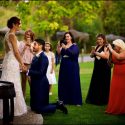 Groom in his knees holding hands with the bride, surrounded by a group of female guests in the party at Quinta da Cheinha, by the wedding photographer in Portugal.