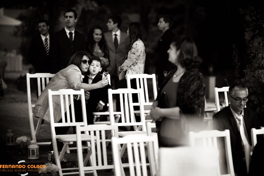 Mother and son, seated in the chairs of the wedding ceremony at Quinta da Serra, take a selfie.