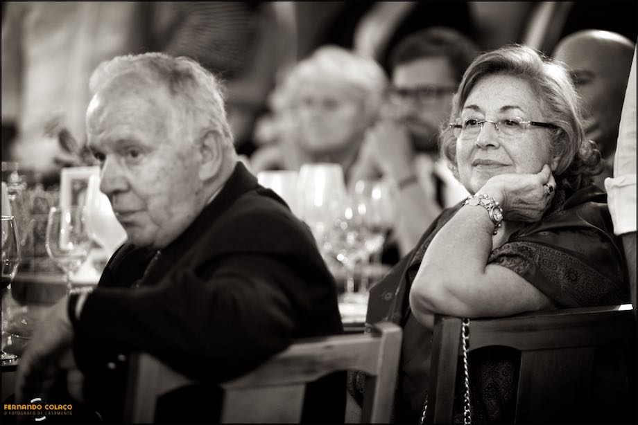 Leaning on the arms of their chairs, two wedding guests watch the film about the newlyweds during the party at Quinta da Cascata.