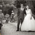 On a dirt road, in the middle of the trees in the countryside, the couple, with children on bicycles passing by, past the wedding photographer in Alentejo.