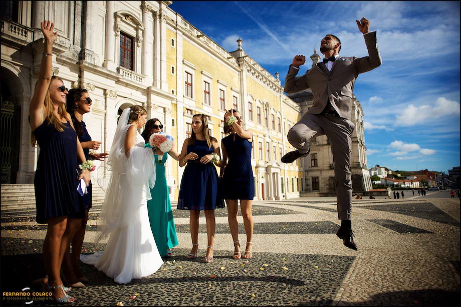 Groom jumps with happiness in front of the bride and friends.