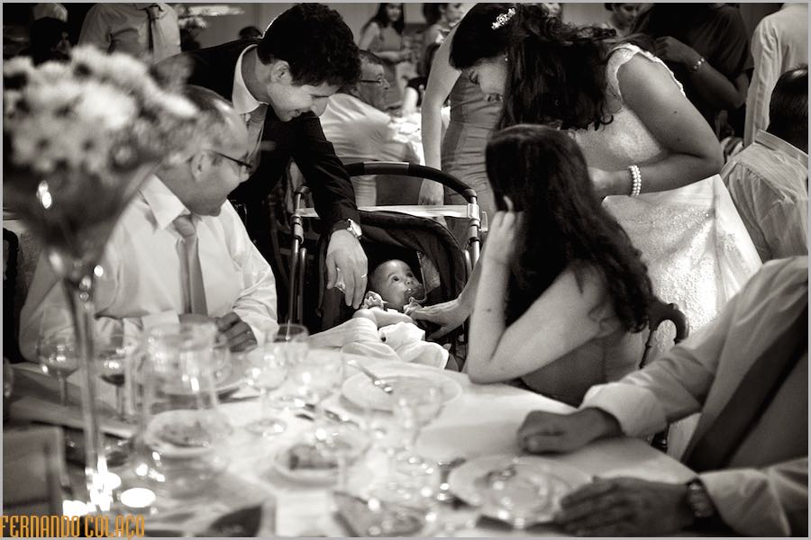 The bride and groom with two guests sitting at the table and looking at the baby, who looks at them.