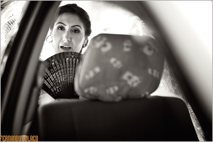 Inside the car to go to the ceremony, the bride refreshes herself with a fan, in a composition by the wedding photographer in Lisbon, Portugal.