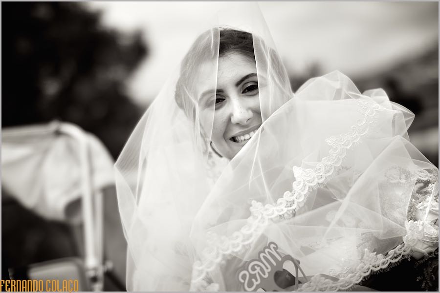 The bride, wrapped in the veil of her wedding dress, smiling in happiness after the wedding ceremony is finished, by the wedding photographer.