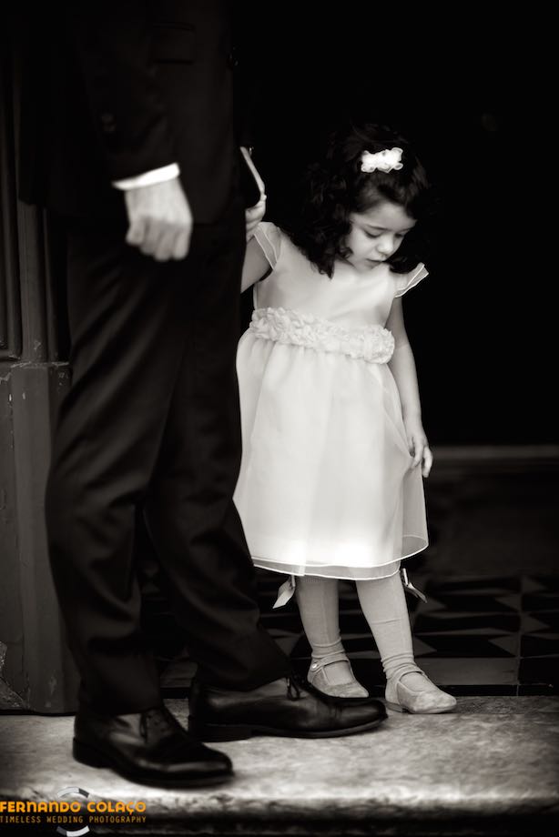 Girl, holding hands with her father, looking at her shoes, outside the church of the wedding ceremony.