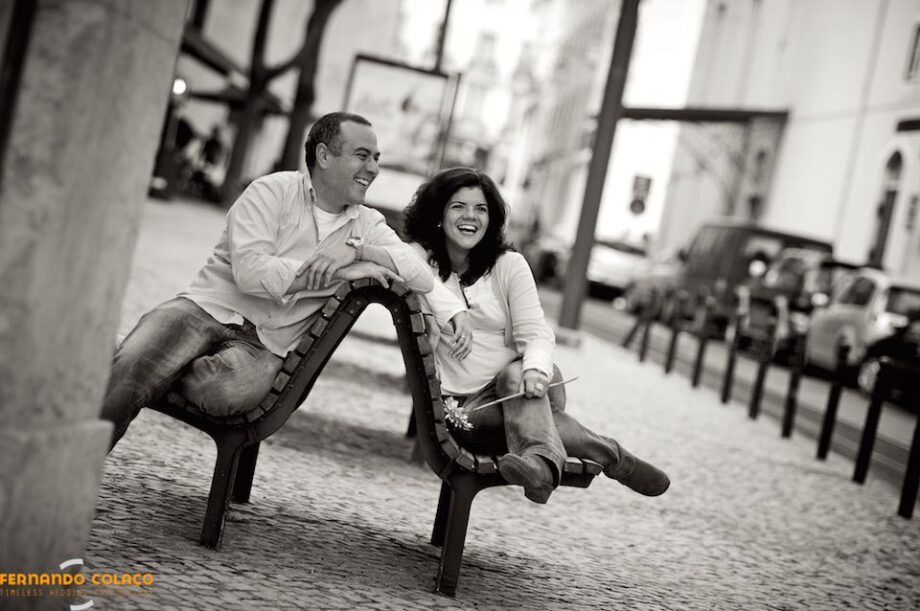 The bride and groom, at the dating session in Chiado, sitting on a double bench, laughing.