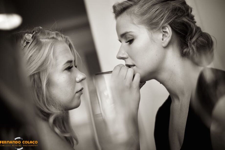 The bride's sister paints her lips, seen in profile by the wedding photographer in Portugal.