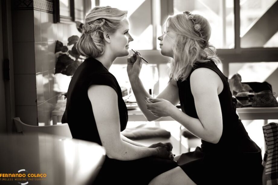 Sitting facing each other, the sister of the bride retouches her lip paint before dressing for the ceremony.