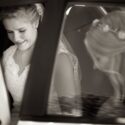Already inside the car to take her to the Church of São Pedro de Penaferrim in Sintra, the bride smiles when her sister, out of focus, helps her with her dress, seen by the wedding photographer.