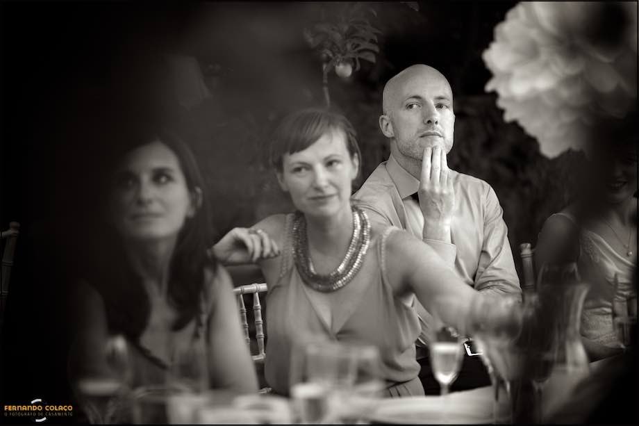 Among family members seated at the table, the groom listens attentively to someone giving a speech.