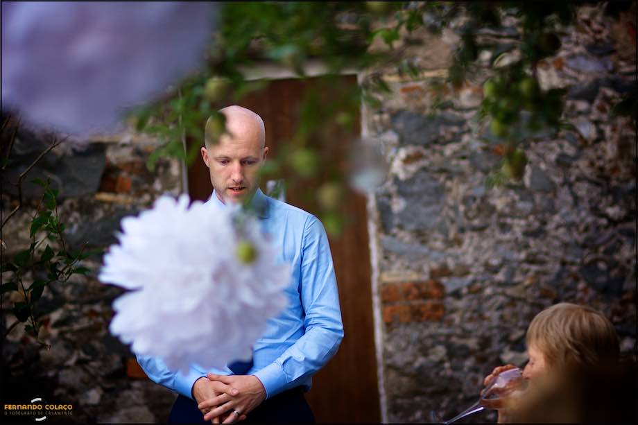 Behind decorations hanging from a tree, the groom gives a speech at his wedding dinner.