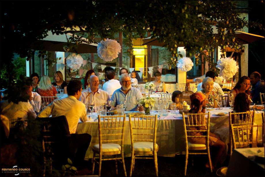 Guests seated at the table at the wedding party, under the orange light of the lamps, in an old Villa in Monchique.