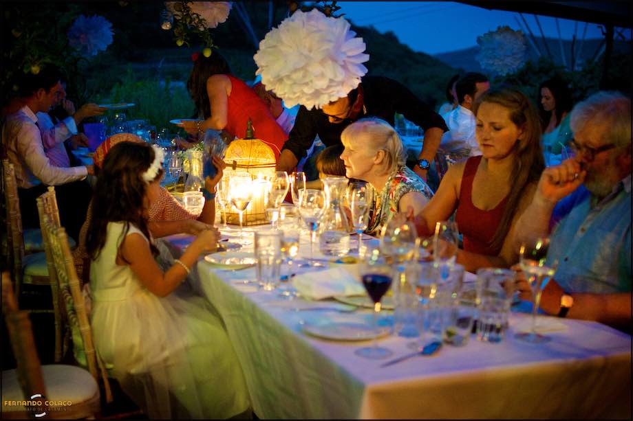 Wedding guest chatting with another, seated at table together with others under the warm light of the decor lamps.