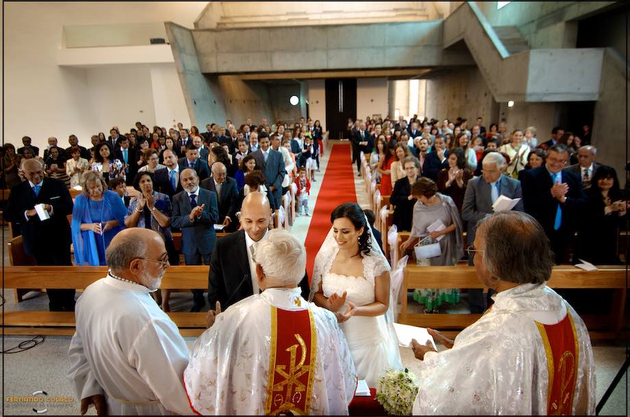 With three priests in front of them and all the guests behind them, the bride and groom at the end of the wedding ceremony in the Church of s: Francisco de Assis in Restelo, seen by the wedding photographer in Lisbon.