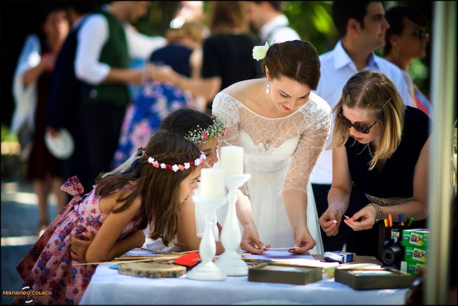 The bride, next to two girls and a lady, checks a card on a table, captured by the wedding photographer at Quinta da Serra in Sintra.