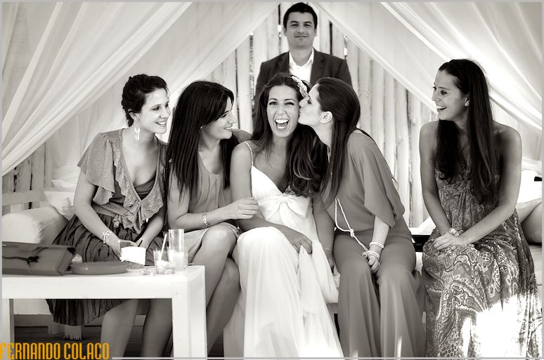 Sentada, num banco do Waikiki na Praia da Sereia, a noiva recebe carinhos e felicitações das suas amigas, vistas pelo fotógrafo de casamento em Lisboa.