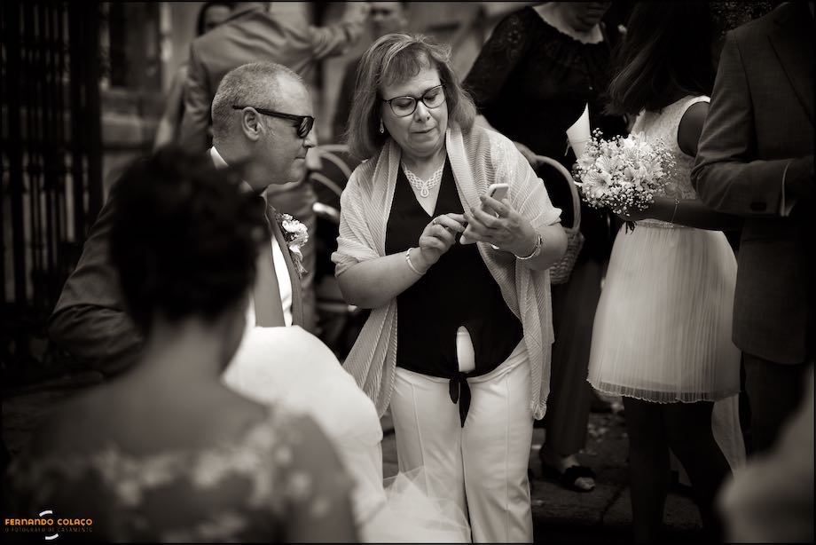 Uma convidada do casamento explica algo a um amigo num telemóvel, na saída da igreja antes da partida para a festa do casamento.