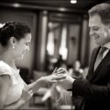 Os noivos, sorridentes, vistos de perfil quando o noivo entrega a aliança do casamento à noiva no Hotel Palácio Estoril.