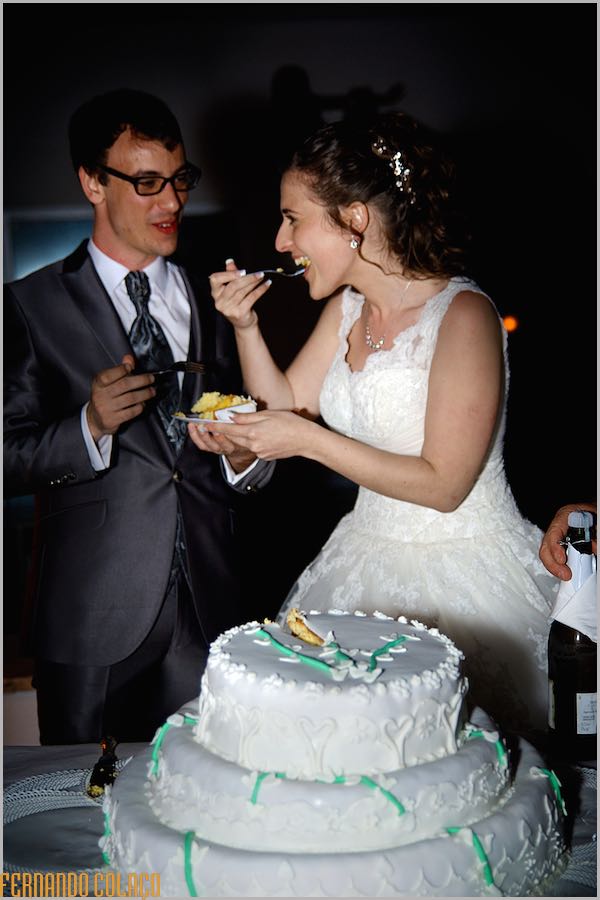 A noiva, junto do noivo, prova o bolo do casamento, vistos pelo fotógrafo de casamento em Évora.