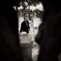 A noiva com o pai quando seguem para o local da cerimónia do casamento, vistos por entre o tronco de uma oliveira no Castelo de S. Jorge, pelo fotógrafo de casamento em Lisboa.