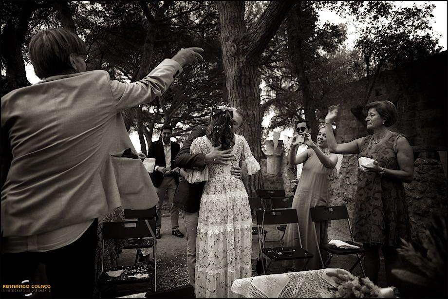O pai do noivo e a mãe da noiva atiram flores os noivos enquanto eles se abraçam, felizes por ter terminado a cerimónia do casamento, visto pelo fotógrafo de casamento em Lisboa.