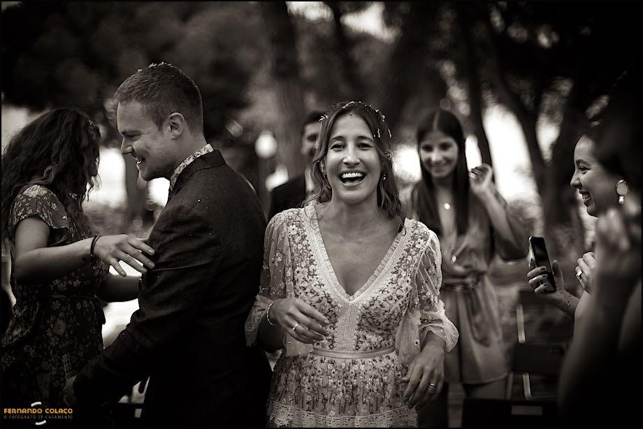 A noiva, junto do noivo que olha para outro lado, ri muito para alguém à sua frente, rodeada pelos familiares que estiveram com eles na cerimónia do casamento, conforme confirma o fotógrafo de casamento Lisboa.