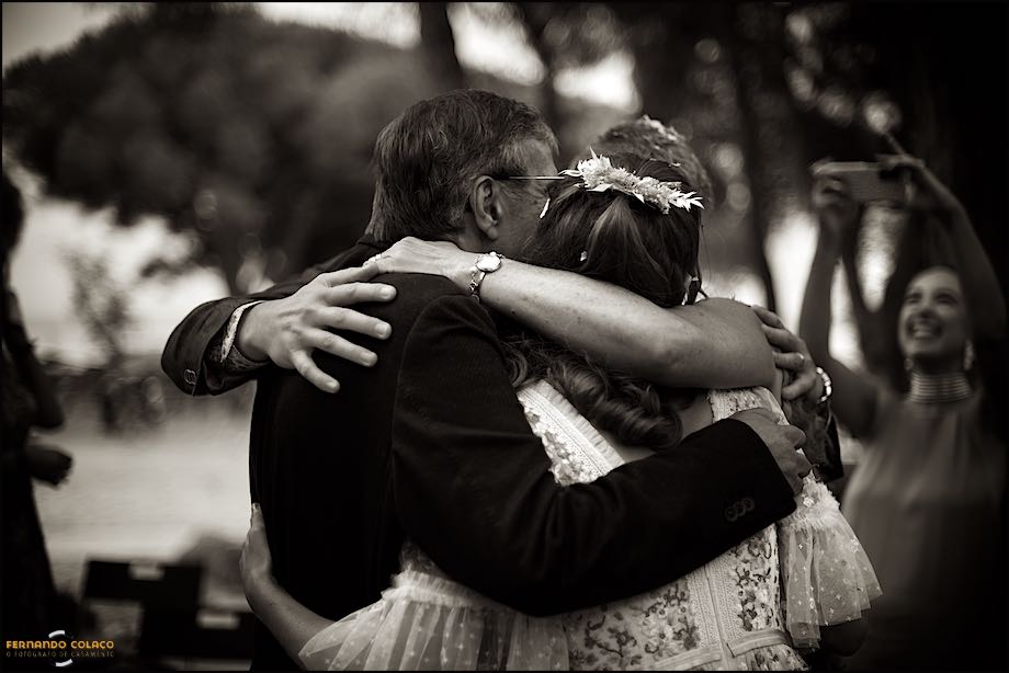 Vários braços abraçando a noiva enquanto estão ser fotografados por uma convidada depois da cerimónia do casamento, vistos por detrás pelo fotógrafo de casamento no Castelo de S. Jorge em Lisboa.