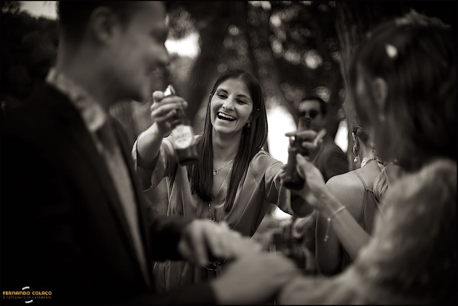 Vista por entre os noivos desfocados, a irmã da noiva oferece-lhe duas cervejas para festejar o facto de estarem já casados, pelo fotógrafo de casamento em Portugal.