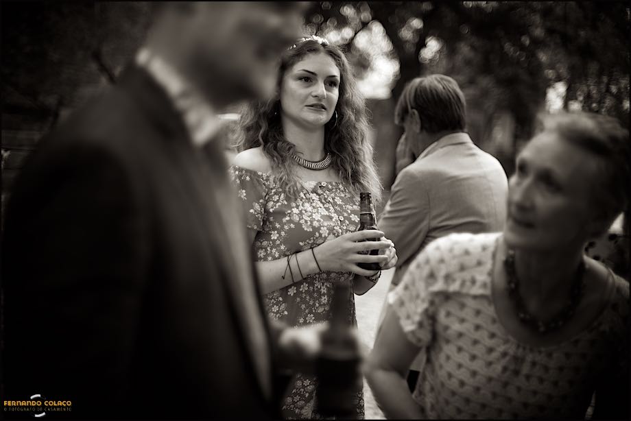 A irmã do noivo segurando uma cerveja quando festejava o casamento, vista entre ele e a mãe, desfocados, pelo fotógrafo de casamento no Castelo de S. Jorge em Lisboa.
