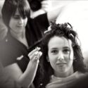 Com a cabeleireira por detrás dela, a noiva num espelho durante o penteado para a cerimónia, numa composição do fotógrafo de casamento em Braga.