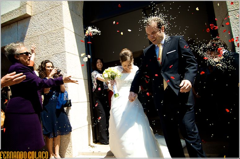Os noivos saem da igreja sob grãos de arroz e pétalas atiradas pelo seus convidados que os esperavam na porta, pelo fotógrafo de casamento em Lisboa.