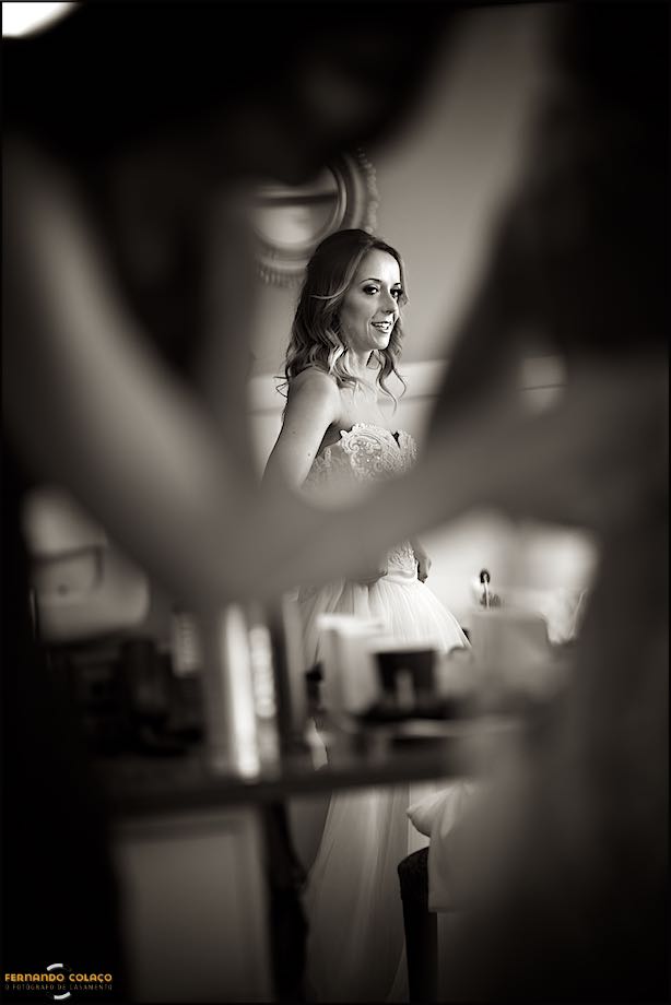 A noiva vista num espelho por entre os braços dela e de uma amiga que a ajuda com o vestido, numa composição do fotógrafo de casamento em Cascais no Grande Real Villa Itália Hotel & Spa.