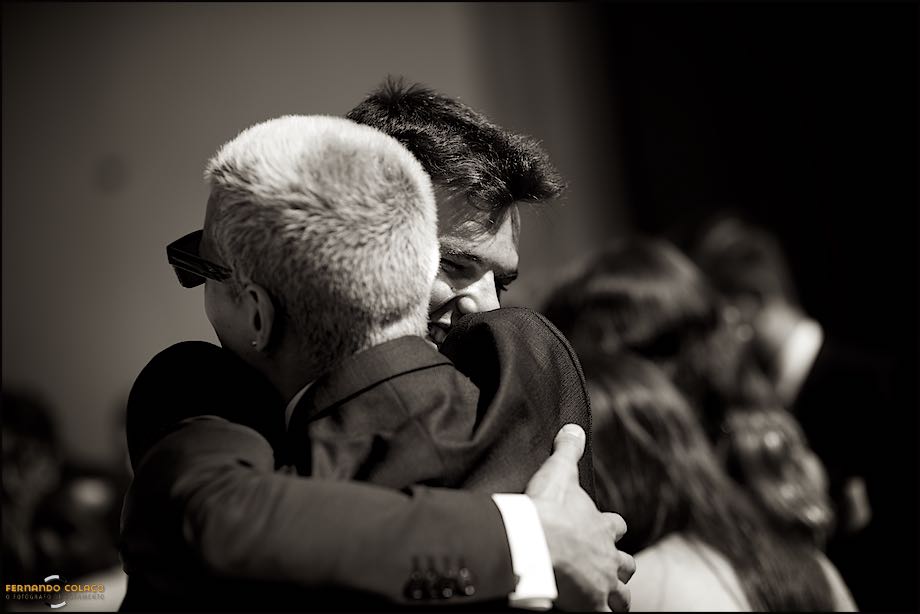 O noivo abraçando um convidado que o felicita, quando saem da igreja no fim da cerimónia do casamento, vistos pelo fotógrafo de casamento em Cascais.
