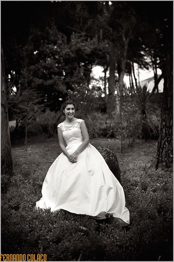 No meio das grandes árvores do jardim da Quinta do Lumarinho, a noiva, sentada sobre uma grande rocha.