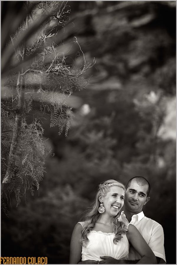 No jardim na Praia Grande em Ferragudo, o noivo abraça a noiva por detrás e ambos riem, num retrato pelo fotógrafo de casamento no Algarve.