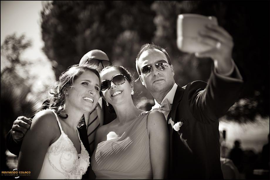 Durante o convívio depois da cerimónia do casamento nos Pézinhos no Tejo, os noivos fazem uma selfie com dois convidados, vistos pelo fotógrafo de casamento em Lisboa.